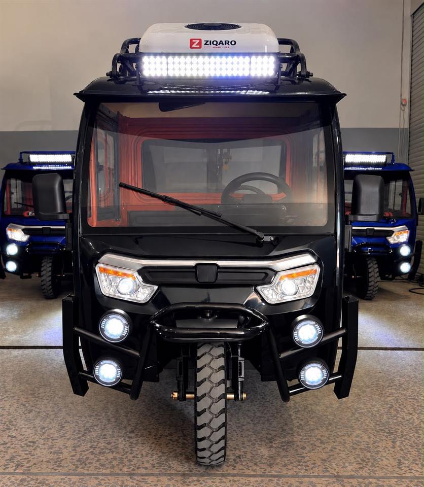 Triciclo Hércules de frente, con cabina cerrada, aire acondicionado en el techo y luces encendidas